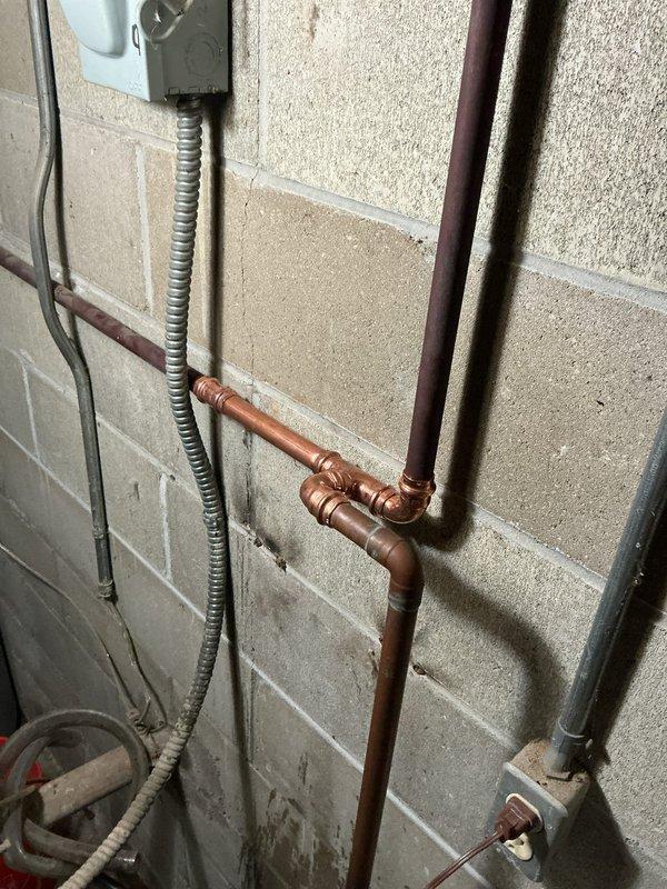 Removed existing water softener unit and reworked copper water supply lines to restore proper water flow throughout the residence. Installed new copper piping configuration with compression fittings and 90-degree elbows, ensuring secure mounting to concrete block wall and proper alignment with existing electrical conduit and utility systems.