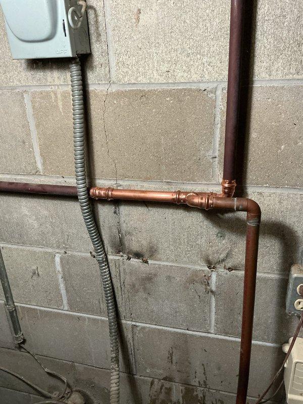 Removed existing water softener unit and reworked copper water supply lines to restore proper water flow throughout the residence. Installed new copper piping configuration with compression fittings and 90-degree elbows, ensuring secure mounting to concrete block wall and proper alignment with existing electrical conduit and utility systems.