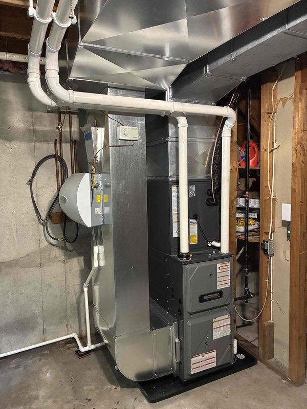 Completed full HVAC system installation including new furnace unit in basement mechanical room and outdoor condensing unit. Furnace installed against foundation wall with proper ductwork connections to existing metallic supply plenum and white PVC venting routed through ceiling area. Exterior AC unit positioned on concrete pad with refrigerant line set and electrical disconnect mounted to exterior wall, conduit run completed, and all connections properly secured and tested for operation.
