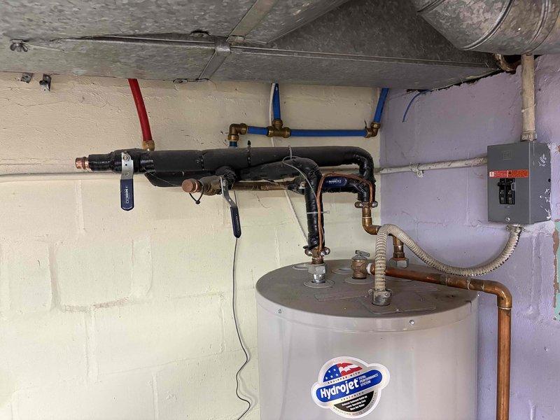 Conducted on-site assessment for tankless gas water heater replacement estimate. Existing 9-year-old HydroJet conventional storage water heater currently installed with standard plumbing connections, water treatment system, and electrical components. Documented current installation configuration including copper piping, shut-off valves, flexible connectors, and associated mechanical components to provide accurate specifications for tankless conversion requirements.