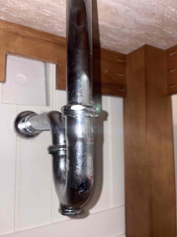 Completed replacement of bathroom sink drain assembly including P-trap and tailpiece connections. Removed existing worn components and installed new chrome tailpiece with black plastic P-trap assembly, ensuring proper alignment and secure coupling nut connections to prevent leaks.
