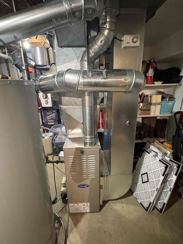 Completed full furnace installation in basement utility room, installing new Carrier brand heating unit with proper positioning and ventilation access. Installed and connected metallic ductwork system throughout the space, including vertical and horizontal runs with elbow joints and proper fastening to ensure efficient airflow distribution. System tested and verified operational with new air filter installed.