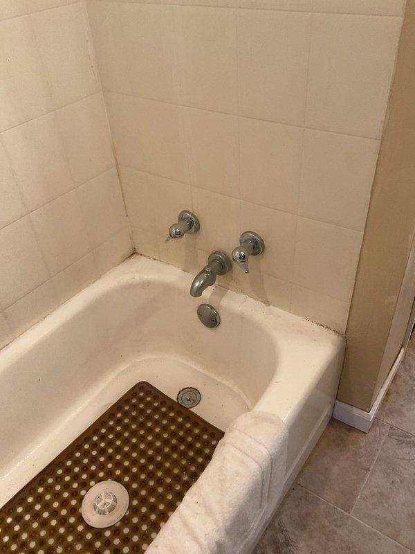 Responded to service call for multiple plumbing issues including plugged drains, severely restricted water flow from faucets due to calcium buildup, and an active leak in the garage with potential source originating from basement area. Inspected bathroom fixtures showing mineral deposits on chrome fittings and tub hardware, as well as corroded brass elbow fitting in utility space exhibiting significant yellow-green corrosion and deterioration at connection points. Documented conditions with photos for estimate preparation and provided assessment of required repairs.