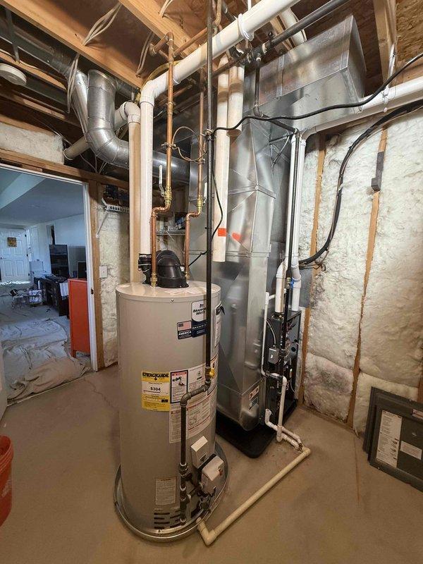 Completed full installation of new HVAC furnace and water heater system in basement utility area. Installed rectangular HVAC unit with metallic finish, connected refrigerant lines along wall studs, and routed silver metallic ductwork from unit. Installed cylindrical water heater with white PVC venting piping, mounted circulator pump on top, and connected all necessary plumbing lines. All systems tested and operational upon completion.