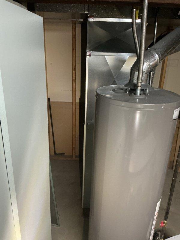 Conducted furnace estimate for club member at operational system scheduled for midday appointment. Documented existing HVAC equipment in basement utility area, including current furnace unit with standard ventilation configuration and associated ductwork system. Photographed equipment layout showing furnace positioned adjacent to water heater with metallic ductwork, insulated horizontal and vertical ducts, and proper venting connections in unfinished basement space with concrete flooring and exposed structural elements.