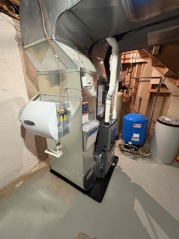 Completed full HVAC system installation including new furnace and air conditioning condenser unit. Installed furnace in basement mechanical room on protective mat with proper clearances, connected white PVC exhaust and intake venting routed vertically through structure, and integrated white humidifier unit to left side of furnace cabinet. Ran copper refrigerant lines from furnace to exterior, secured with mounting brackets. Installed outdoor AC condenser unit on level concrete pad in backyard, connected refrigerant lines and electrical disconnect box mounted to exterior wall. Configured metallic supply ductwork from furnace plenum, routed through ceiling joists. Verified all electrical connections, tested system operation, confirmed proper airflow and refrigerant charge levels, and ensured all safety controls functioning correctly.