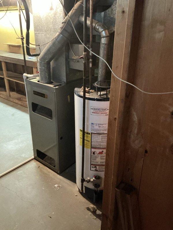 Completed full HVAC system assessment for furnace and air conditioning replacement at unoccupied residential property undergoing preparation for occupancy. Both systems confirmed to be approximately 25 years old and located in basement utility area. Evaluated existing equipment configuration including ductwork layout, electrical connections, and venting arrangements. Documented current installation with photographs showing gray metal furnace unit with black ductwork extending upward, adjacent water heater, concrete floor space, and exposed wooden wall framing with various pipes and wiring. Assessed aged metal ductwork system featuring multiple elbows and bends with visible dust accumulation throughout basement space. Provided comprehensive replacement estimate for complete HVAC system upgrade.