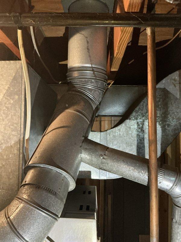 Completed full HVAC system assessment for furnace and air conditioning replacement at unoccupied residential property undergoing preparation for occupancy. Both systems confirmed to be approximately 25 years old and located in basement utility area. Evaluated existing equipment configuration including ductwork layout, electrical connections, and venting arrangements. Documented current installation with photographs showing gray metal furnace unit with black ductwork extending upward, adjacent water heater, concrete floor space, and exposed wooden wall framing with various pipes and wiring. Assessed aged metal ductwork system featuring multiple elbows and bends with visible dust accumulation throughout basement space. Provided comprehensive replacement estimate for complete HVAC system upgrade.