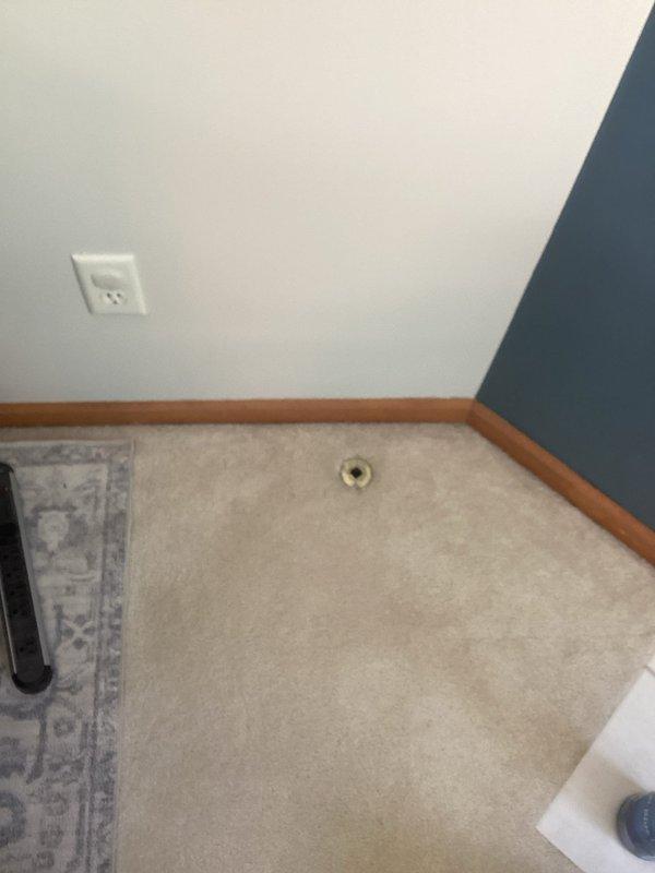 Responded to gas odor complaint originating from fireplace key valve area. Upon inspection, identified gas leak at floor-mounted gas valve assembly with decorative cover plate. Documented existing conditions with photographs showing valve location in carpeted area and close-up of brass Dante valve cover with evidence of gas migration through keyhole opening. Recommended immediate valve replacement or repair to eliminate leak hazard and restore safe operation of fireplace system.