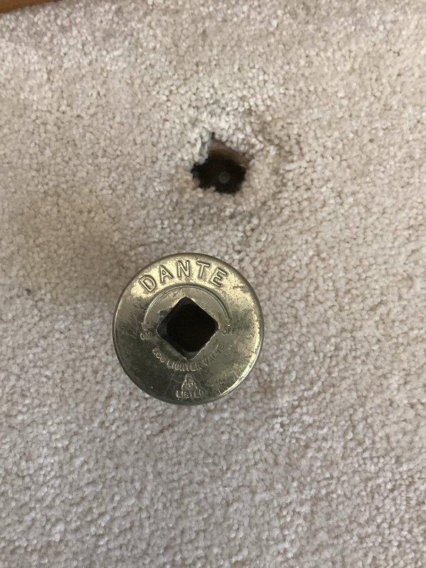 Responded to gas odor complaint originating from fireplace key valve area. Upon inspection, identified gas leak at floor-mounted gas valve assembly with decorative cover plate. Documented existing conditions with photographs showing valve location in carpeted area and close-up of brass Dante valve cover with evidence of gas migration through keyhole opening. Recommended immediate valve replacement or repair to eliminate leak hazard and restore safe operation of fireplace system.