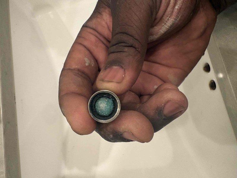 Responded to no water complaint at residential property with history of water heater issues. Upon inspection, discovered severely clogged faucet aerators throughout home causing reduced water flow that appeared as complete water loss. Removed and examined shower trim valve and multiple faucet aerators, finding significant mineral buildup and sediment deposits restricting water passage. Cleaned aerator screens showing blue-green corrosion and mineral accumulation. Restored water flow to affected fixtures by clearing blockages and reinstalling components.