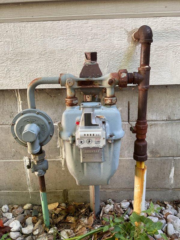 Completed on-site evaluation for tankless water heater replacement estimate at single-family residence. Assessed existing water heater installation in basement, documented current gas meter configuration showing significant corrosion on inlet/outlet connections and upper piping, and evaluated utility infrastructure including pressure regulator and gas supply lines. Photographed basement plumbing configuration with exposed framing, existing water supply pipes, and shut-off valves to determine feasibility and requirements for tankless conversion installation.
