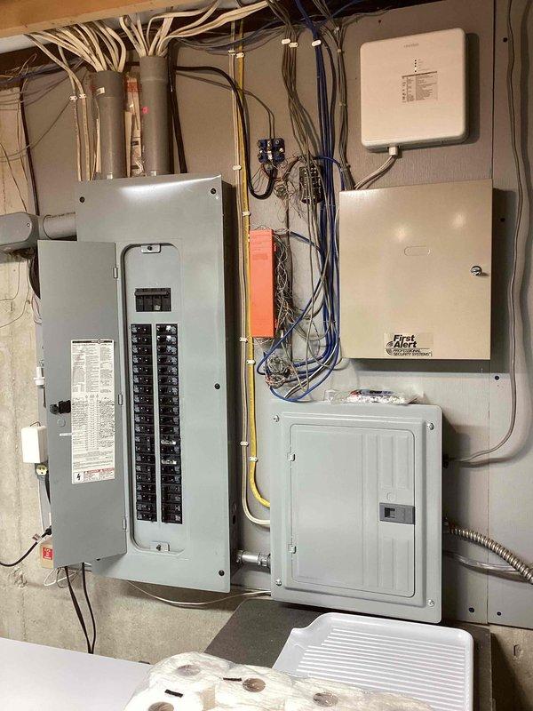 Completed generator estimate and furnace tune-up on a 7-year-old heating system. Documented existing HVAC ductwork installation in attic space, including gray cylindrical supply ducts, flexible duct branches, and metal plenum with access panel. Photographed electrical panel configuration showing main breaker panel with dual rows of circuit breakers, associated sub-panels, and integrated communication equipment for comprehensive system assessment.