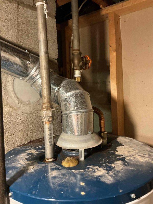 Responded to service call for leaking water heater in basement utility area. Upon inspection, identified active leak on existing white cylindrical unit with blue top and expansion tank assembly. Evaluated plumbing connections, including metallic supply lines, PVC discharge piping, and shut-off valves. Documented current installation showing signs of deterioration with visible moisture, staining, and drip patterns on tank surface. Provided estimate for complete water heater replacement due to compromised tank integrity.
