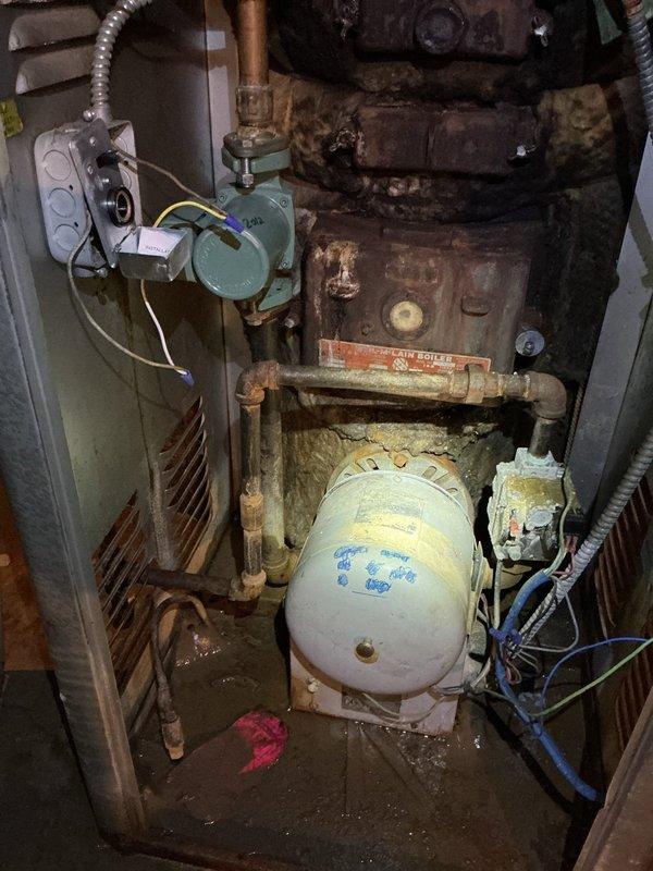 Responded to no hot water complaint on 15-year-old water heater system. Upon inspection, found aging tank-style water heater with significant corrosion on piping and connections, along with visible rust on tank exterior. Assessed mechanical equipment area containing water heater, circulator pump assembly with copper piping, and associated plumbing infrastructure showing advanced deterioration. Documented equipment condition with photographs showing weathered components, oxidized pipes, and moisture staining on concrete floor indicating potential past leakage. Evaluated overall system age and wear patterns consistent with equipment nearing end of service life.