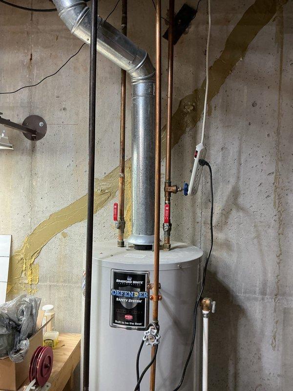 Responded to service call for leaking 12-year-old Bradford White water heater with Defender Safety System. Upon inspection, identified active leak and documented condition of unit and surrounding plumbing connections including copper supply lines, brass fittings, and pressure relief valve. Based on age of equipment and observed conditions, provided assessment and recommendations to customer.