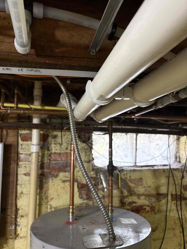 Completed full furnace installation in basement mechanical room. New gray furnace unit was installed on black protective pad with proper PVC venting routed to exterior and metallic ductwork connected to existing distribution system. All equipment properly secured, labeled, and tested for safe operation alongside existing water heater.
