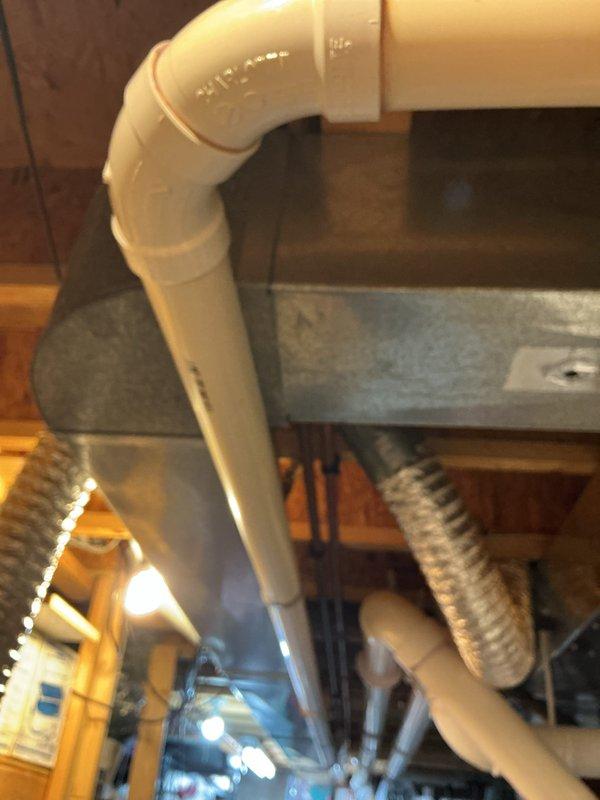 Responded to emergency call for loud explosion sound from water heater with water detected in drain pan. Inspected 16-year-old water heater system and associated plumbing connections. Evaluated condition of copper supply lines, PVC venting configuration, and recirculation pump assembly. Documented existing installation including hot and cold water connections, brass shut-off valves, and mechanical room setup. Photographed HVAC ductwork proximity, pipe routing, and overall system layout. Provided estimate for water heater replacement due to age and reported failure symptoms consistent with tank rupture.
