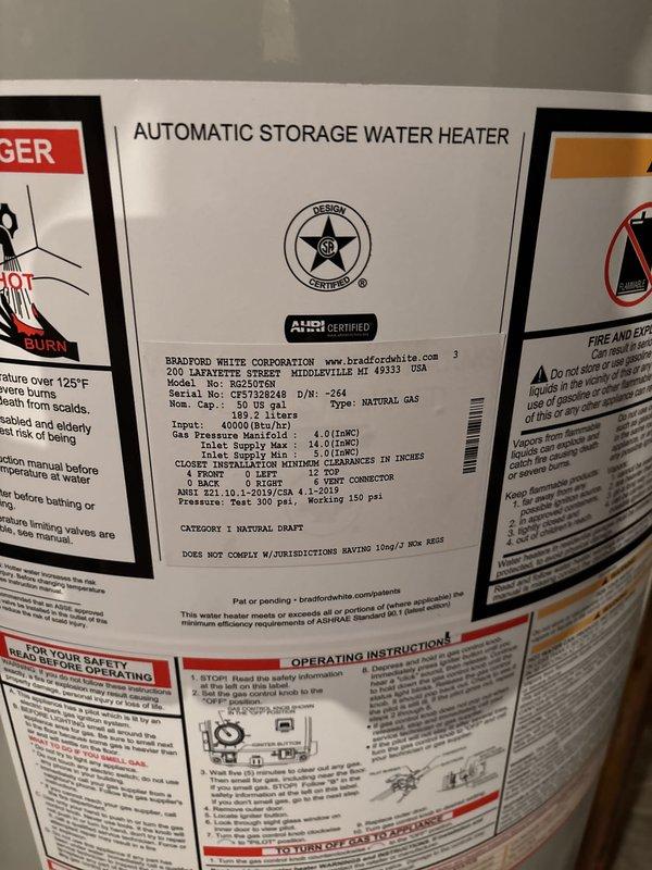 Completed installation of Bradford White residential gas-fired water heater in basement utility room. Installed unit with proper copper piping connections, red shut-off valves on supply lines, and black exhaust vent pipe. Configured gas control assembly and burner access components according to manufacturer specifications. Verified all safety labels, technical specifications, and regulatory compliance information are properly displayed on unit. Installation meets clearance requirements and industry standards for residential gas water heating equipment.
