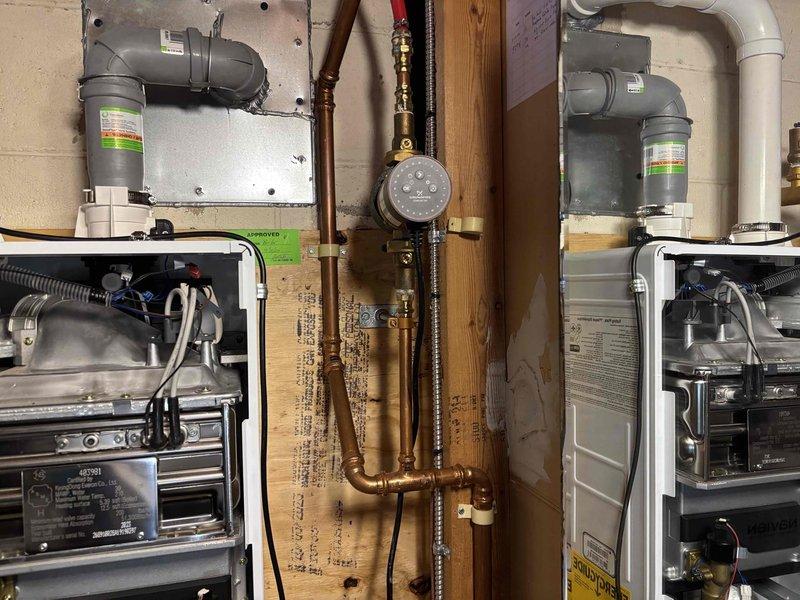 Responded to complaint of insufficient hot water delivery to fixtures in residential property with two-year-old Navien tankless water heater system. Upon inspection, found dual heating units with hydronic manifold configuration and complex copper piping distribution system. Evaluated system pressures using existing gauge, checked all ball valves and zone controls for proper operation, and verified expansion tank functionality. Inspected burner assemblies and internal components of both units with panels open to assess combustion efficiency and heat exchanger condition. Examined copper pipe routing and connections throughout the manifold system to identify any restrictions or flow issues affecting hot water distribution. Verified proper venting through corrugated flexible tubing connections. Adjusted system parameters and confirmed adequate hot water flow to all fixtures upon completion.