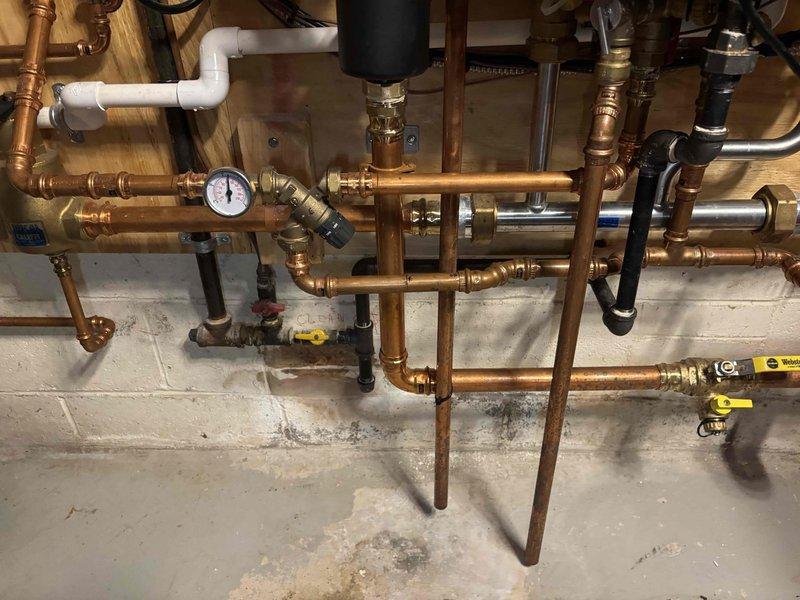 Responded to complaint of insufficient hot water delivery to fixtures in residential property with two-year-old Navien tankless water heater system. Upon inspection, found dual heating units with hydronic manifold configuration and complex copper piping distribution system. Evaluated system pressures using existing gauge, checked all ball valves and zone controls for proper operation, and verified expansion tank functionality. Inspected burner assemblies and internal components of both units with panels open to assess combustion efficiency and heat exchanger condition. Examined copper pipe routing and connections throughout the manifold system to identify any restrictions or flow issues affecting hot water distribution. Verified proper venting through corrugated flexible tubing connections. Adjusted system parameters and confirmed adequate hot water flow to all fixtures upon completion.