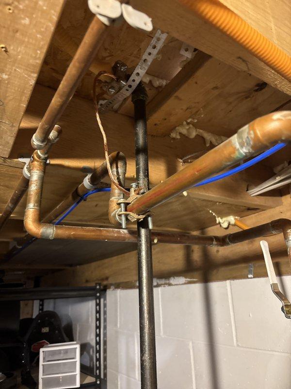 Completed full water heater installation in basement utility area. Removed existing unit and installed new residential cylindrical water heater on concrete floor against cinder block foundation wall. Connected copper supply and discharge lines to top of unit with proper fittings and soldered joints. Installed pressure relief valve with discharge piping per code requirements. Routed all plumbing connections through exposed floor joists above, securing lines with appropriate strapping and brackets. Verified all connections for proper operation and tested unit for leaks.