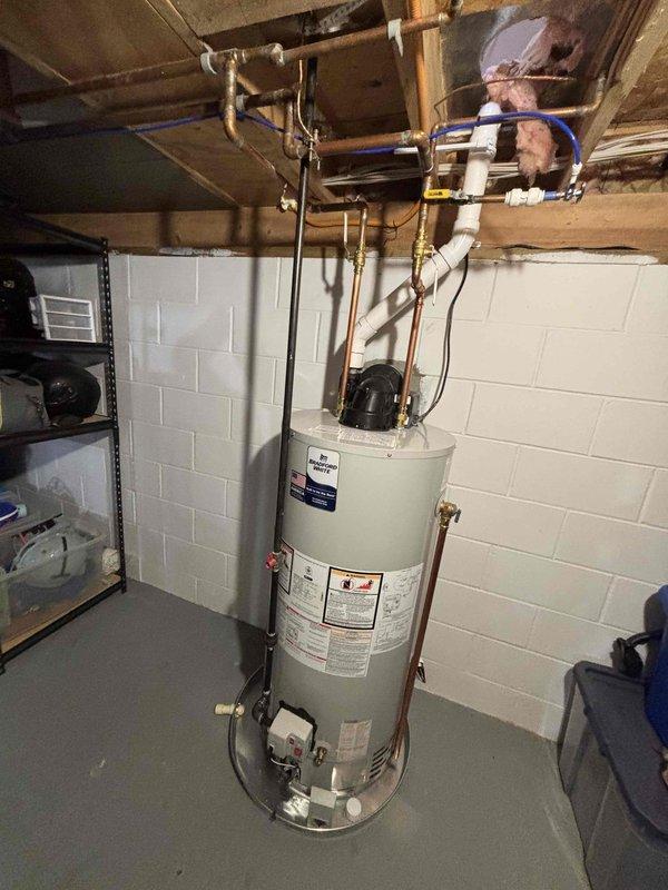Completed full water heater installation in basement utility area. Removed existing unit and installed new residential cylindrical water heater on concrete floor against cinder block foundation wall. Connected copper supply and discharge lines to top of unit with proper fittings and soldered joints. Installed pressure relief valve with discharge piping per code requirements. Routed all plumbing connections through exposed floor joists above, securing lines with appropriate strapping and brackets. Verified all connections for proper operation and tested unit for leaks.