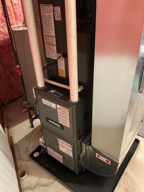 Completed full HVAC system replacement including installation of new furnace, air conditioning unit, and water heater. Interior furnace and water heater installed in basement utility area on protective mat with proper PVC venting, condensate drainage, and gas line connections. Exterior AC unit positioned on ground-level pad with refrigerant lines run through metal conduit along foundation wall, electrical disconnect boxes mounted, and all connections properly secured and tested for operation.