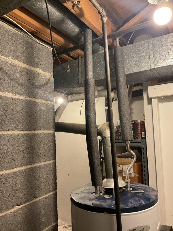Responded to emergency service call for leaking water heater with water supply shut off. Upon arrival, inspected 17-year-old residential water heater located in basement utility area showing active water leakage at base. Unit exhibited age-related deterioration and compromised tank integrity consistent with end of serviceable life expectancy. Documented existing installation configuration including gas connections, venting system, and plumbing connections. Photographed water heater positioning between wooden framing and concrete block walls, noting accessible clearances and utility room layout. Provided estimate for complete water heater replacement including removal of existing failed unit and installation of new equipment to restore hot water service to residence.
