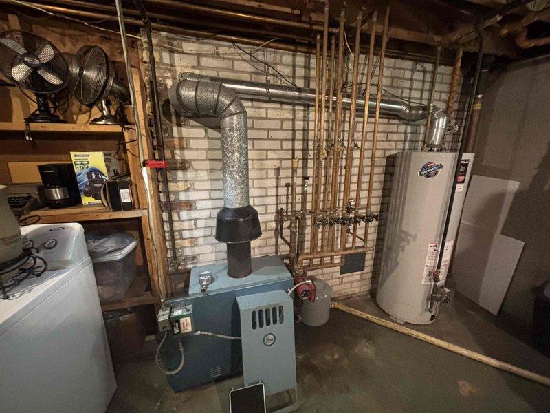 Responded to a boiler complaint of an abnormal (non-blue) burner flame and failure to maintain set temperature on a cast-iron, gas-fired hydronic boiler of approximately 50 years in age. Inspected the unit, venting, and associated components, including the draft hood and flue, circulator pump, expansion tank, and control and wiring connections, and observed floor staining and discoloration around the base of the boiler and aged copper piping joints with soldering residue. Based on the unit's age, combustion and performance issues, and visible signs of deterioration, discussed replacement options with the homeowner.