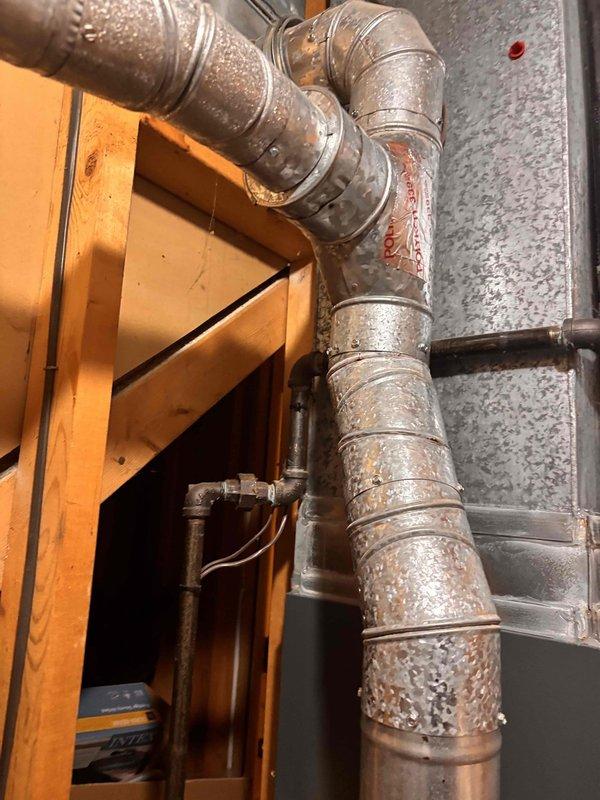 Performed annual heating tune-up on 22-year-old Bryant furnace and inspected the galvanized flue vent pipe for the surface crack reported by the gas company. Observed scattered surface corrosion and oxidation along the vent pipe sections, particularly near the band joints and seams, with no obvious separation or major damage visible; connections remain secured with metal bands and fasteners. Recommend continued monitoring of the vent pipe condition and consideration of vent replacement as the corrosion progresses.