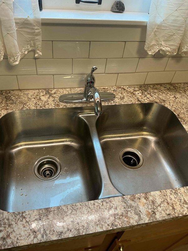 Installed a new chrome single-handle gooseneck faucet on the center deck plate of the double-basin stainless steel kitchen sink, securing the mounting hardware and connecting the hot and cold supply lines. Tested for proper operation, flow, and temperature control, confirmed no leaks at the connections, and verified drainage at both basins.