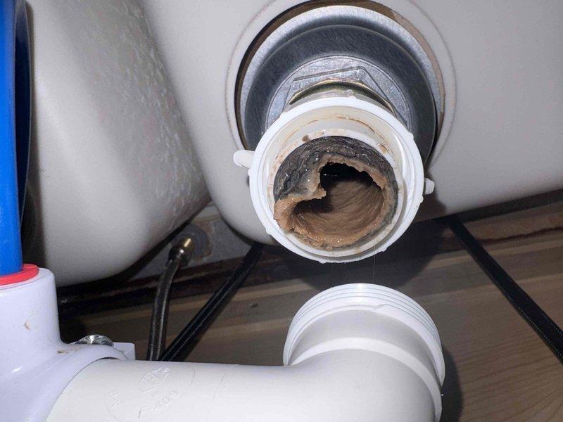 Inspected the double-basin sink where one basin was draining poorly and found the drain tailpiece and trap fitting heavily fouled with thick sludge, grease, and mineral buildup that restricted flow. Disconnected the affected drain assembly, cleaned and cleared the obstruction, and inspected the connections, gasket, and flexible hose for proper seating. Reassembled the fittings and confirmed the basin now drains freely with no leaks.