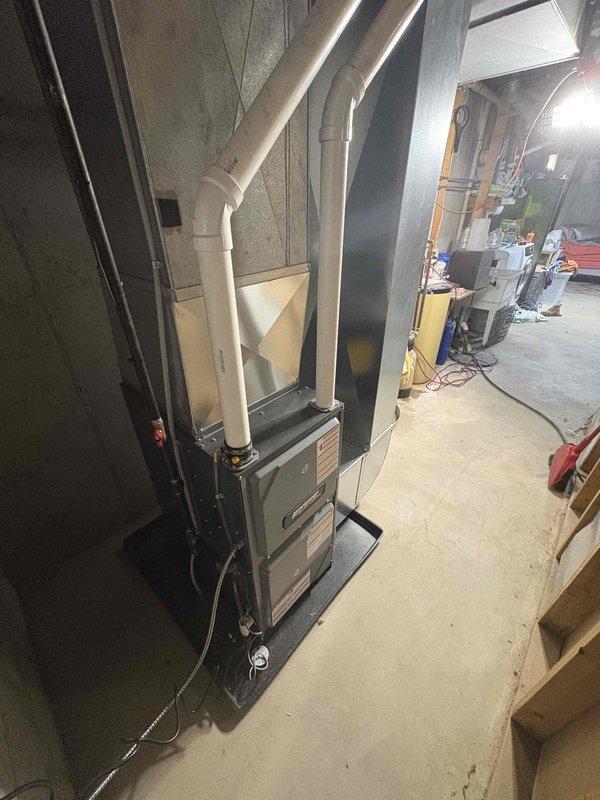 Installed a new high-efficiency upright gas furnace on a drain pan in the basement utility area, with PVC intake/exhaust venting routed overhead and connected to a galvanized supply plenum and existing ductwork. Completed electrical connections via flexible conduit, labeled the plenum, and verified the installation showed no visible damage or defects.