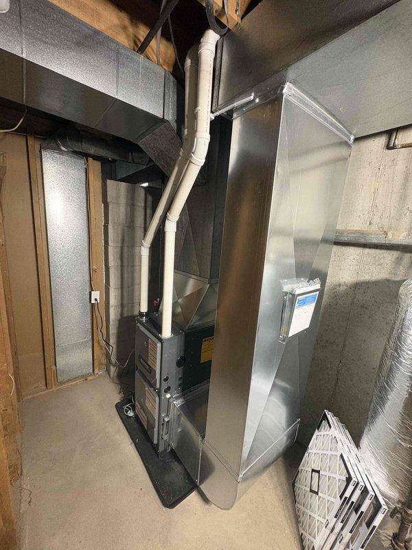 Installed a new high-efficiency upright gas furnace on a drain pan in the basement utility area, with PVC intake/exhaust venting routed overhead and connected to a galvanized supply plenum and existing ductwork. Completed electrical connections via flexible conduit, labeled the plenum, and verified the installation showed no visible damage or defects.
