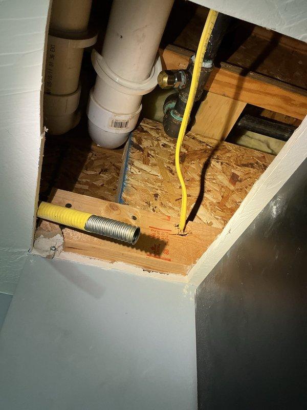 Responded to a reported gas leak after the utility had shut off service and a prior pressure test failed to locate the source. Opened the drywall ceiling to inspect the concealed gas piping and found a corrugated stainless steel tubing (CSST) run terminating abruptly with an exposed, uncapped end at the floor framing, indicating a compromised line and the likely leak source. Documented the condition of the CSST, adjacent corroded black iron piping, and brass fittings with photos. The unsafe section should be isolated and repaired or replaced, followed by a pressure test before gas service is restored.