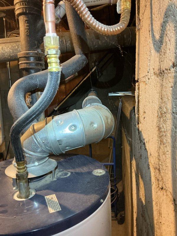 Performed an on-site assessment and estimate for replacement of an existing Whirlpool atmospheric-vent water heater. Inspected the tank, draft hood, and galvanized flue, noting dented vent piping with discoloration, flexible water connectors, and heavy rust and corrosion on the adjacent cast iron pipe and threaded coupling. Documented the installation conditions with photos to support recommendations for the new unit installation, including venting and piping upgrades.