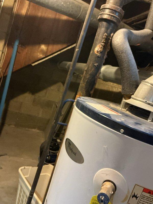 Performed an on-site assessment and estimate for replacement of an existing Whirlpool atmospheric-vent water heater. Inspected the tank, draft hood, and galvanized flue, noting dented vent piping with discoloration, flexible water connectors, and heavy rust and corrosion on the adjacent cast iron pipe and threaded coupling. Documented the installation conditions with photos to support recommendations for the new unit installation, including venting and piping upgrades.