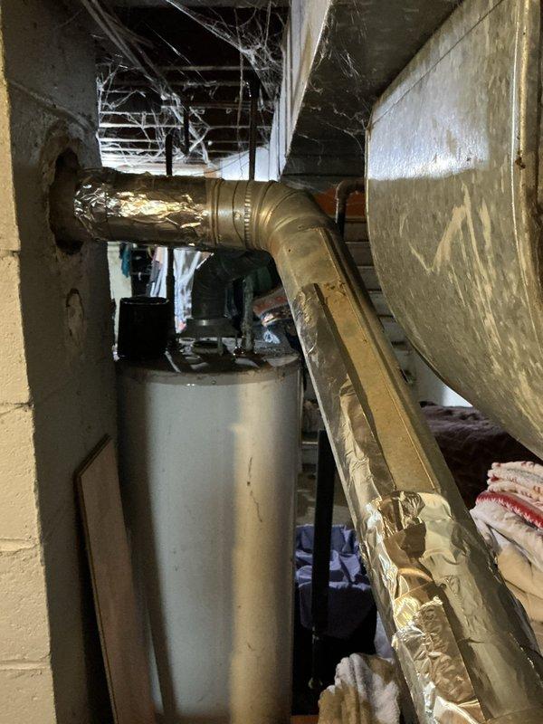 Performed an on-site estimate for furnace replacement on a club member's system following a failed heat exchanger diagnosis. Inspected the gas-fired furnace, flue/venting connections, and adjacent water heater in the basement utility area, noting foil-taped repairs on the galvanized flue piping, and documented existing equipment conditions with photos to support the replacement proposal.