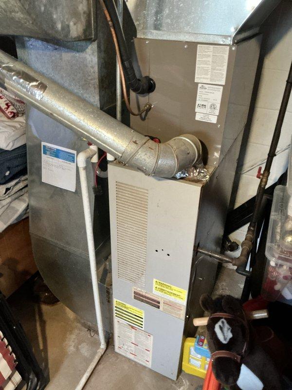 Performed an on-site estimate for furnace replacement on a club member's system following a failed heat exchanger diagnosis. Inspected the gas-fired furnace, flue/venting connections, and adjacent water heater in the basement utility area, noting foil-taped repairs on the galvanized flue piping, and documented existing equipment conditions with photos to support the replacement proposal.