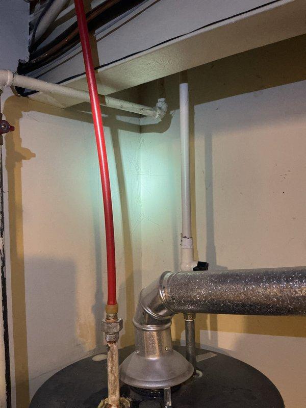 Inspected the existing atmospheric-vent water heater installation and documented conditions to prepare an updated replacement estimate. Noted corrosion and mineral buildup on the threaded brass fittings and supply piping at the tank top, along with flexible aluminum vent connector and draft hood configuration requiring review for code compliance. Also observed a heavily rusted floor drain with deteriorated coating and an aging drain line clamp near the unit, which may require attention during the replacement.