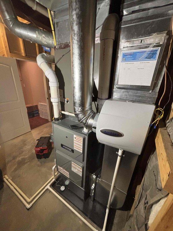 Installed a new upright high-efficiency gas furnace with supply plenum and galvanized ductwork connections, including PVC combustion venting, condensate drain piping, and a flexible gas line connection. Mounted and connected an AprilAire humidifier to the plenum with a dedicated water supply line, and posted the service log sheet on the ductwork for future maintenance records. Completed the installation with a clean, code-compliant mechanical layout and no visible damage or leaks.