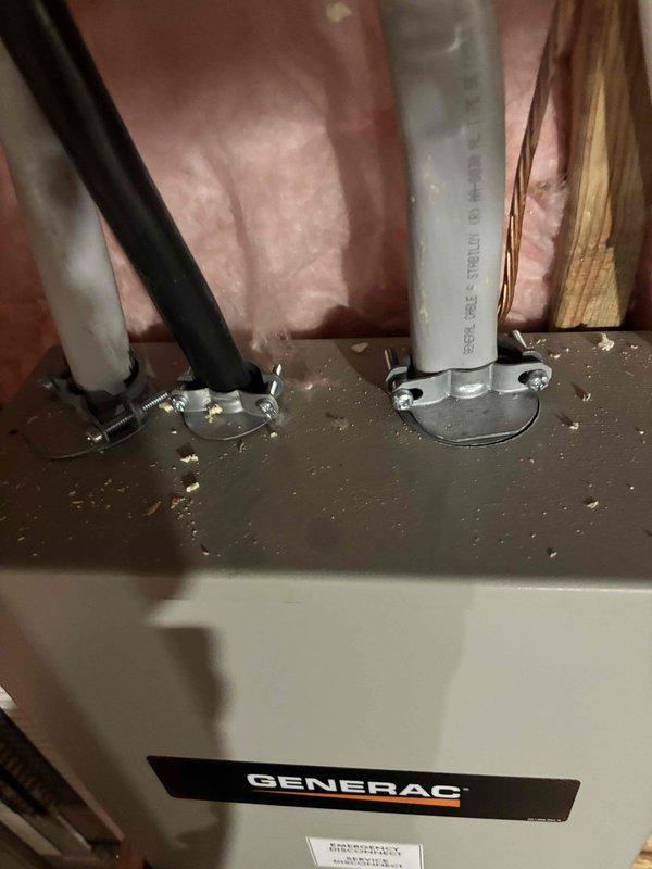 Inspected the installed Generac generator transfer switch/disconnect enclosure and its associated conduit and cable entries to assess the scope of work for relocating the generator. Observed three cable entries (flexible conduit, black conductor cable, and armored cable) secured with clamp connectors, along with a bare copper grounding conductor routed along the framing, and noted wood debris and sawdust on top of the enclosure. Documented existing conditions with photos and prepared a relocation estimate based on the required rerouting and extension of the circuits.