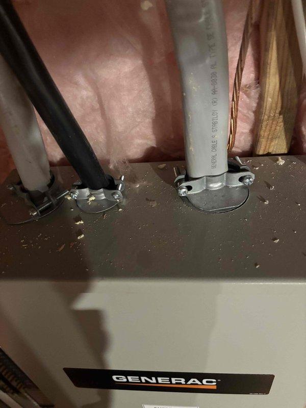 Inspected the installed Generac generator transfer switch/disconnect enclosure and its associated conduit and cable entries to assess the scope of work for relocating the generator. Observed three cable entries (flexible conduit, black conductor cable, and armored cable) secured with clamp connectors, along with a bare copper grounding conductor routed along the framing, and noted wood debris and sawdust on top of the enclosure. Documented existing conditions with photos and prepared a relocation estimate based on the required rerouting and extension of the circuits.