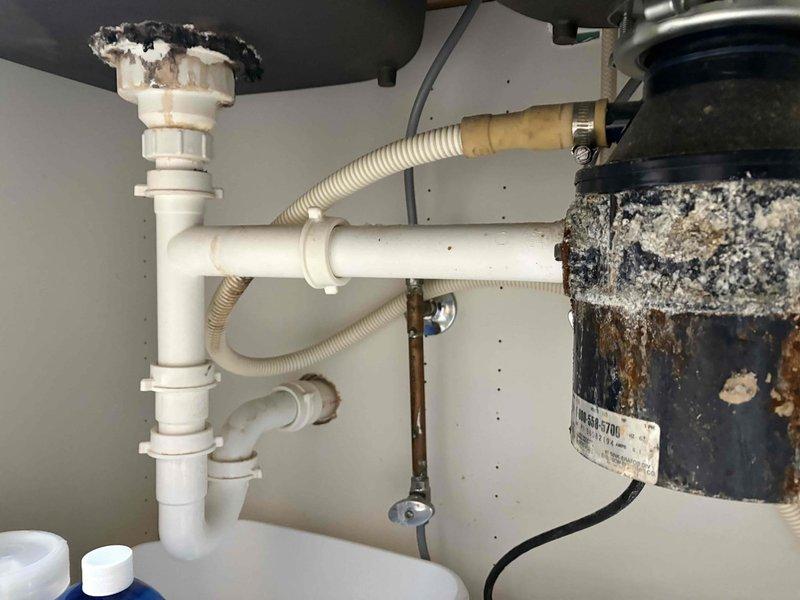 Removed the heavily corroded garbage disposal from beneath the kitchen sink, disconnecting the discharge and drain connections and the electrical supply, and reconfigured the drain assembly. Serviced the water supply line and shutoff valve in the basement, and repaired or replaced the kitchen faucet to restore proper operation.