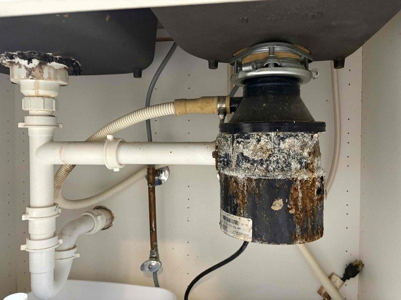 Removed the heavily corroded garbage disposal from beneath the kitchen sink, disconnecting the discharge and drain connections and the electrical supply, and reconfigured the drain assembly. Serviced the water supply line and shutoff valve in the basement, and repaired or replaced the kitchen faucet to restore proper operation.