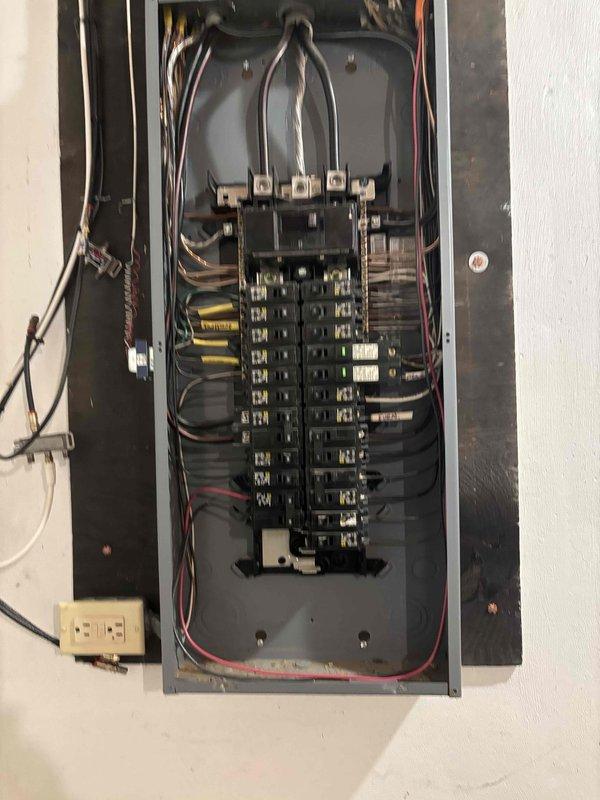 Inspected the main electrical service panel and existing branch circuit wiring to evaluate capacity and feasibility for the requested living room lighting and ceiling fan installation. Observed dense, congested conductor routing within the enclosure and assessed available breaker space and circuit loading to determine the appropriate scope of work. Documented panel conditions with photographs to support quote preparation for the new lighting and fan circuit.