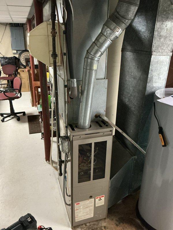 Performed a comprehensive tune-up on a 21-year-old gas furnace, including inspection of the cabinet, flue venting, and ductwork connections, and verification of safe operation. Cleaned accumulated dirt and debris from the equipment area, checked gas piping and controls, and confirmed proper flue connection to the chimney/duct system with no visible corrosion or damage. Also inspected the adjacent water heater, noting the T&P relief discharge, gas control valve, and supply connectors in serviceable condition with no leaks or rust observed.
