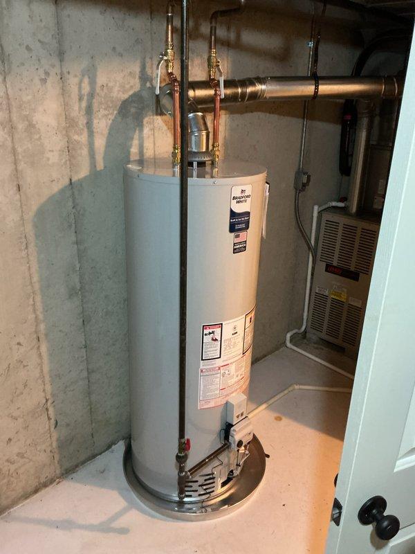 Installed a new Bradford White gas-fired water heater on a metal drain pan, connecting copper supply lines with shutoff valves and tying the draft hood into the existing metal flue vent. Connected the gas control valve and routed the drain line to the existing condensate drain. Verified all connections were secure with no leaks, rust, or damage visible, and left the work area clean and operational.