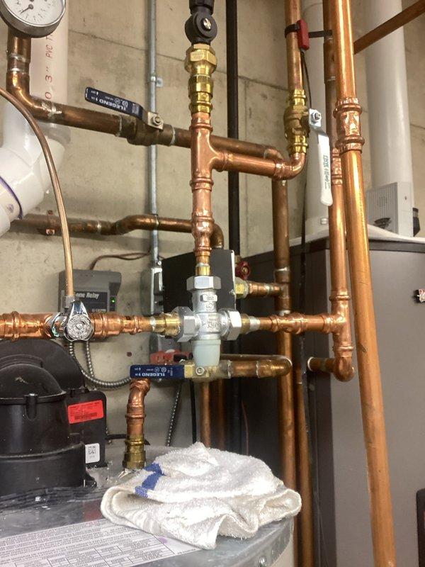 Evaluated a hot water delivery complaint at the master bath, the fixture farthest from the water heater, where hot water is available only briefly. Inspected the mechanical room piping and found a pressed-copper distribution manifold with a multi-port valve assembly and isolation ball valves, and removed a chrome T-fitting that showed heavy mineral and corrosion buildup around its valve cartridge and worn threads, which likely restricts flow. Recommended replacing the corroded fitting and cartridge, and evaluating a hot water recirculation system or rerouting of the supply line to improve hot water delivery to the master bath.